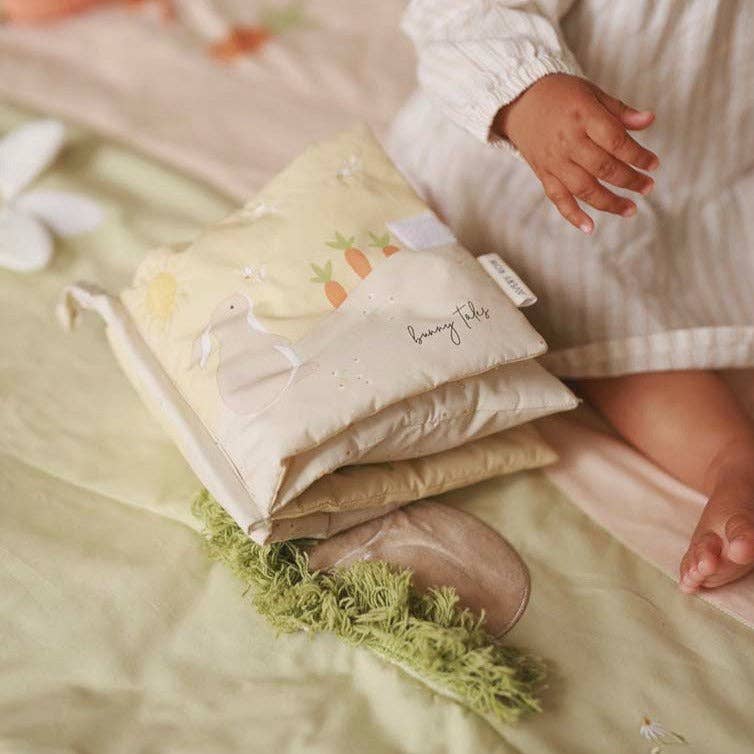 Fabric bunny book with a child's hand reaching towards them on a bed.