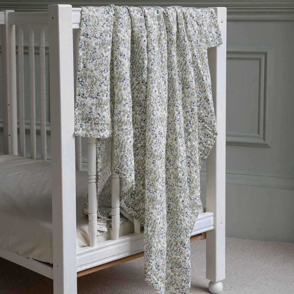 Floral-patterned muslin swaddle draped over a white crib in a room with a gray wall.