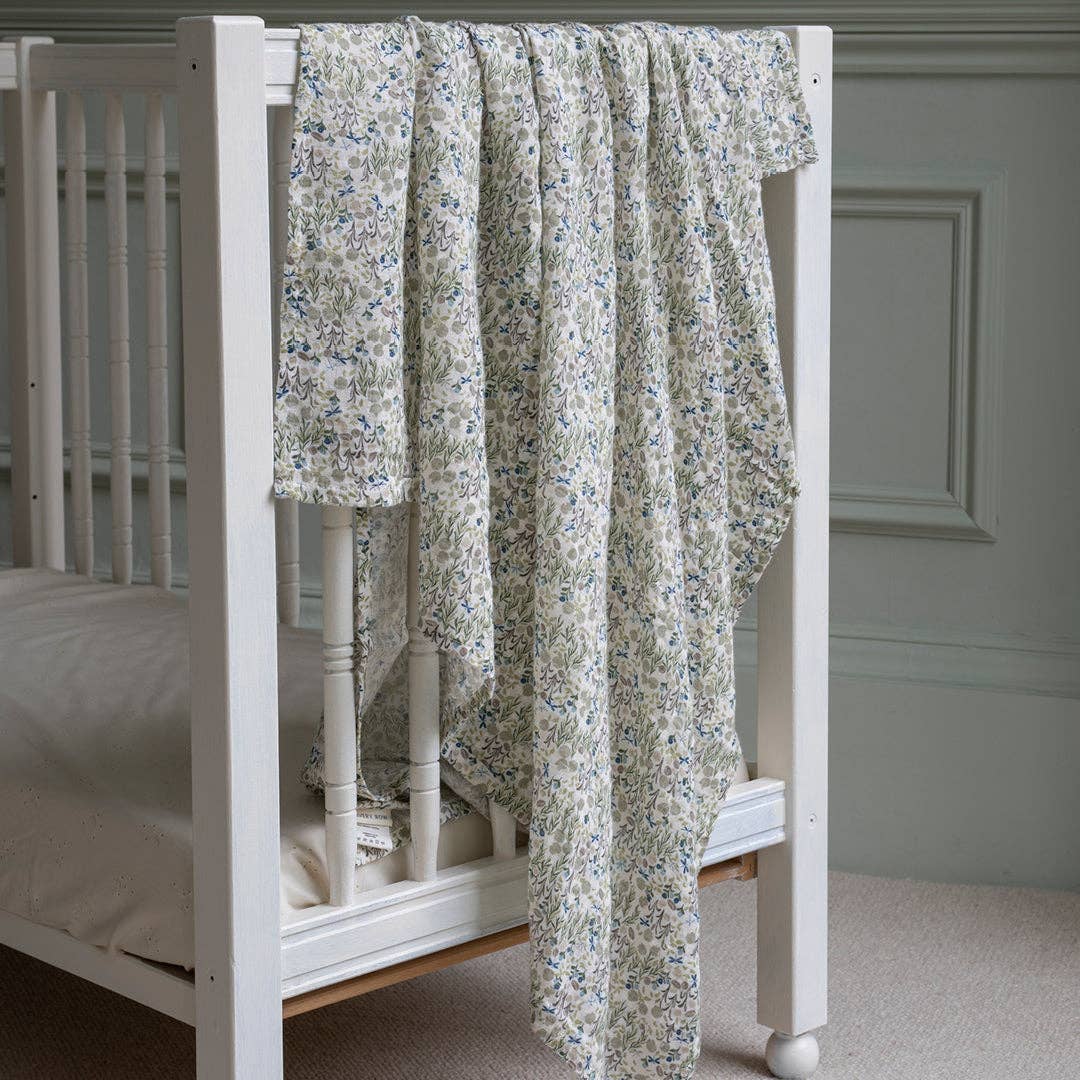 Floral-patterned muslin swaddle draped over a white crib in a room with a gray wall.