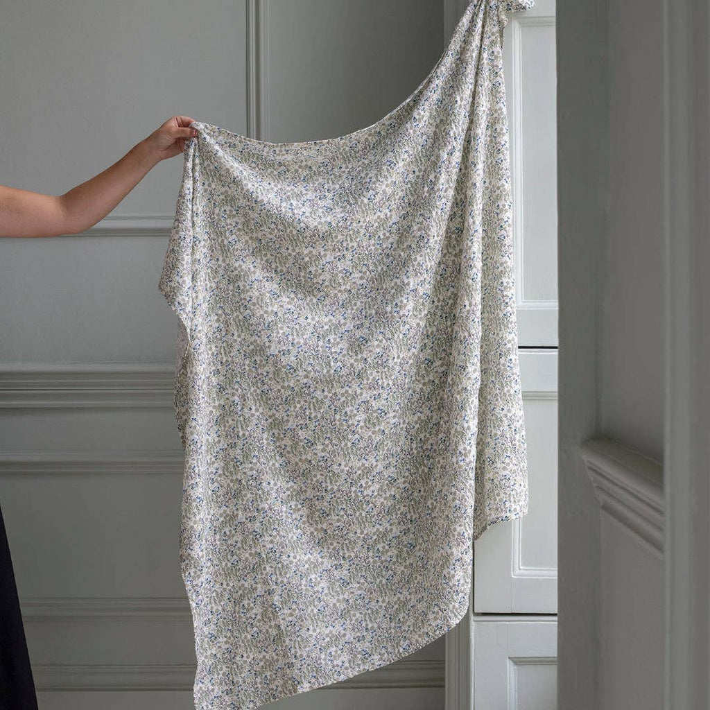 Person holding a floral-patterned fabric in front of a neutral-colored wall.