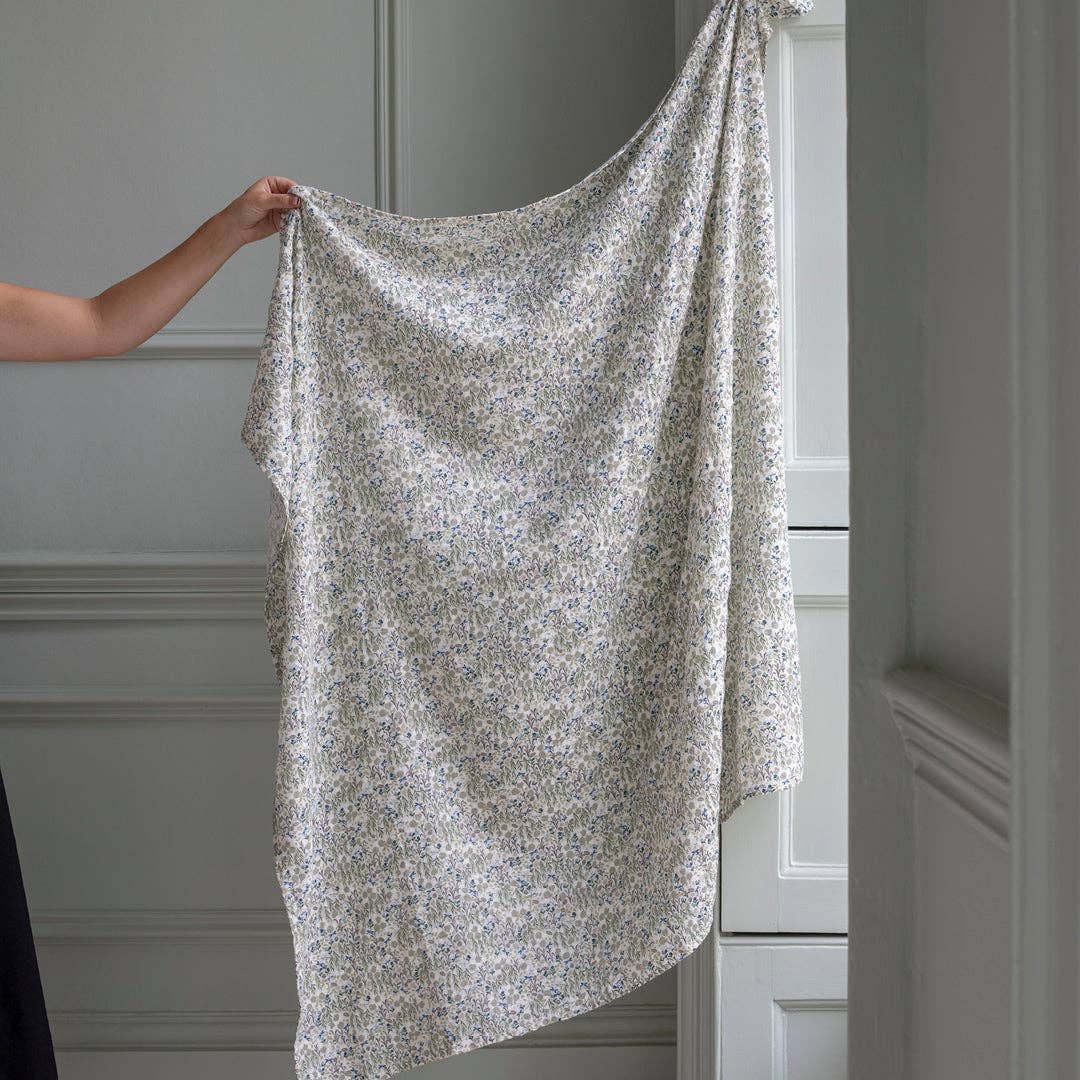 Person holding a floral-patterned fabric in front of a neutral-colored wall.