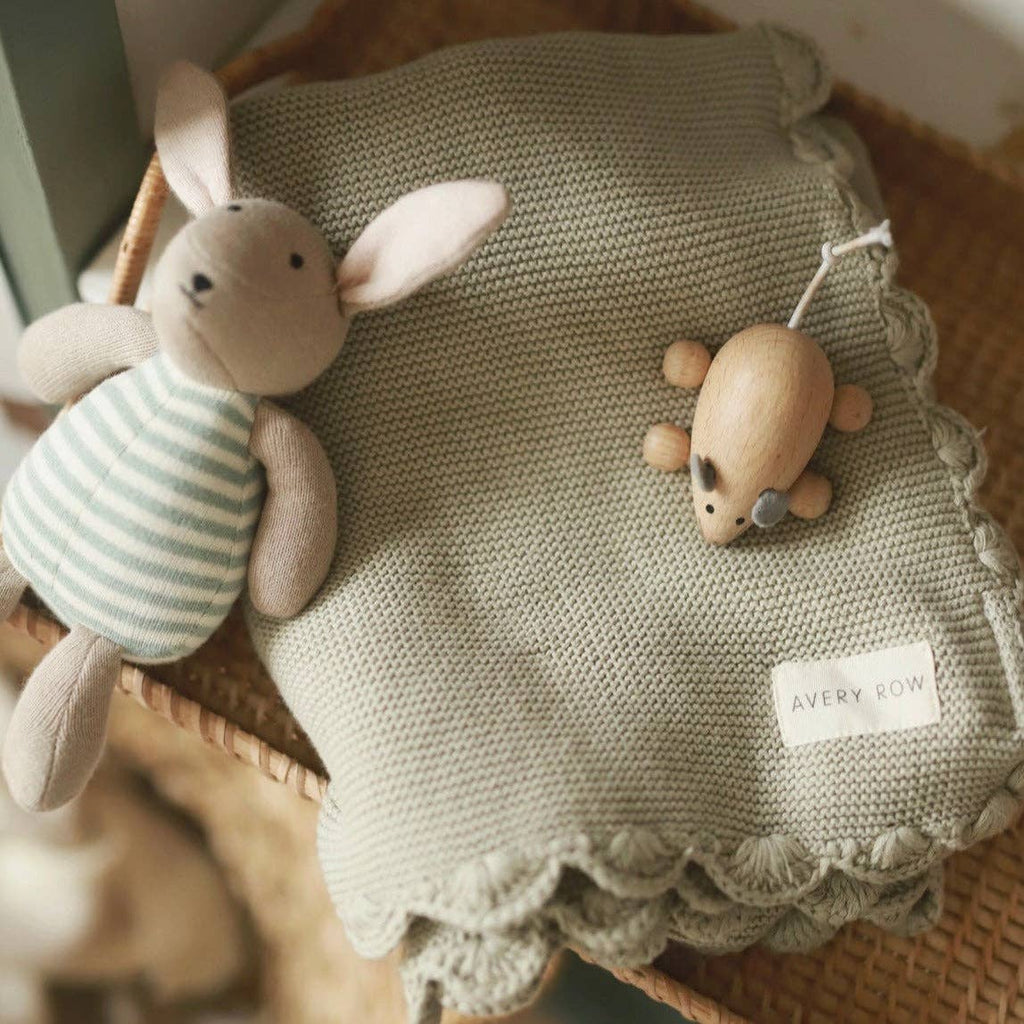 Knitted blanket with a toy rabbit and wooden mouse on a textured surface