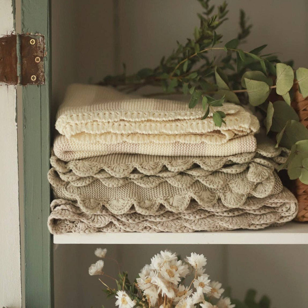 Stack of textured beige blankets on a shelf with greenery and flowers in the background