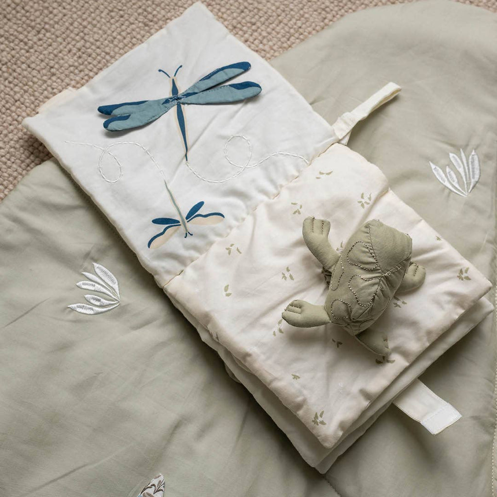 Children's soft book with dragonfly illustrations and a plush turtle toy on a textured surface.