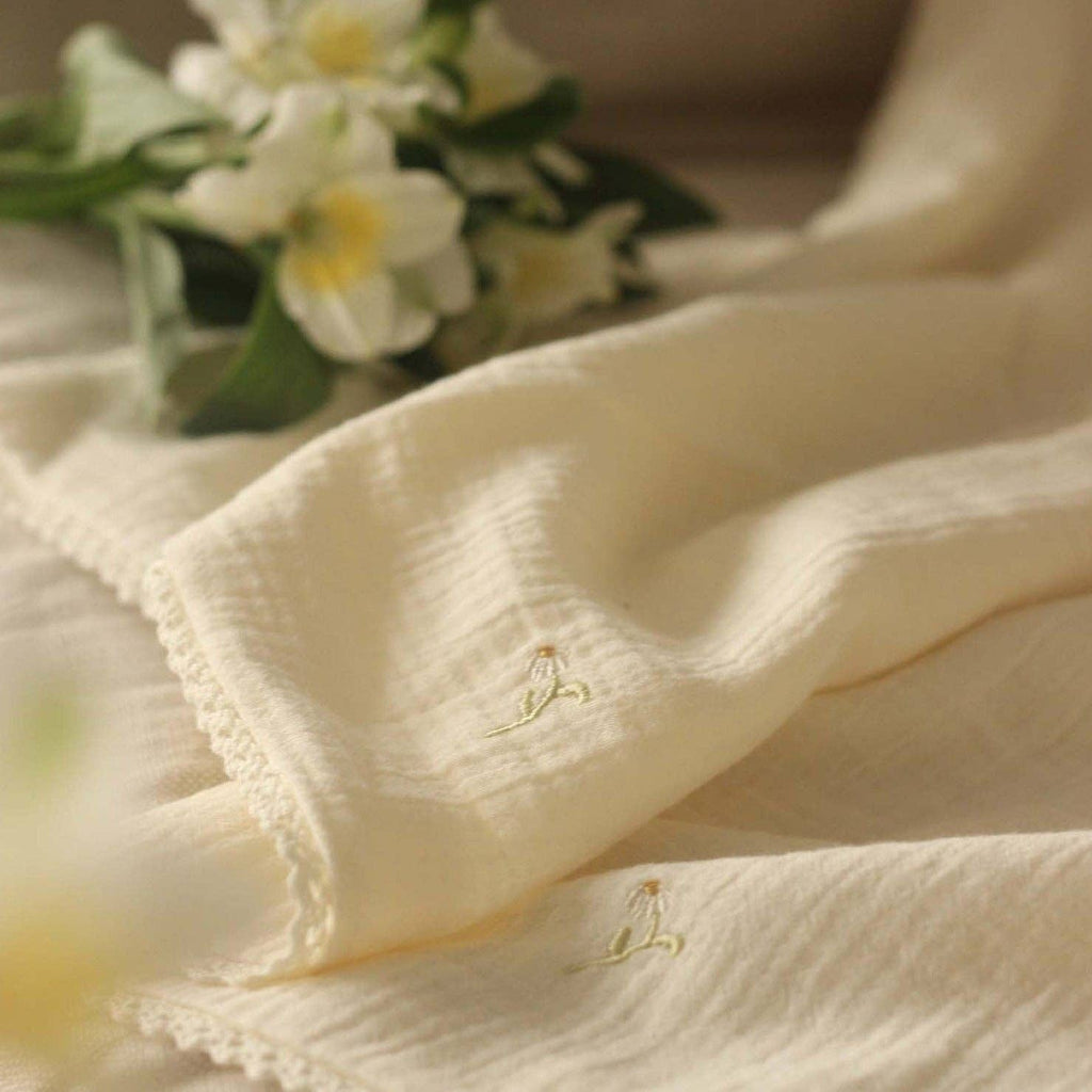 Close-up of muslin blanket with embroidered designs, blurred flowers in the background