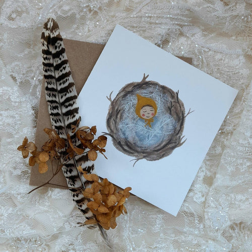 Greeting card with a bird's nest illustration, feather, and dried flowers on a textured surface