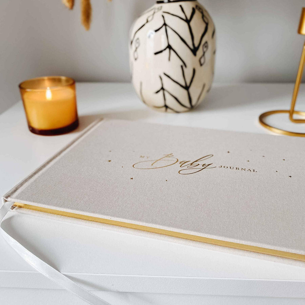 Journal titled 'My Baby Journal' on a white surface with a candle and decorative vase in the background.