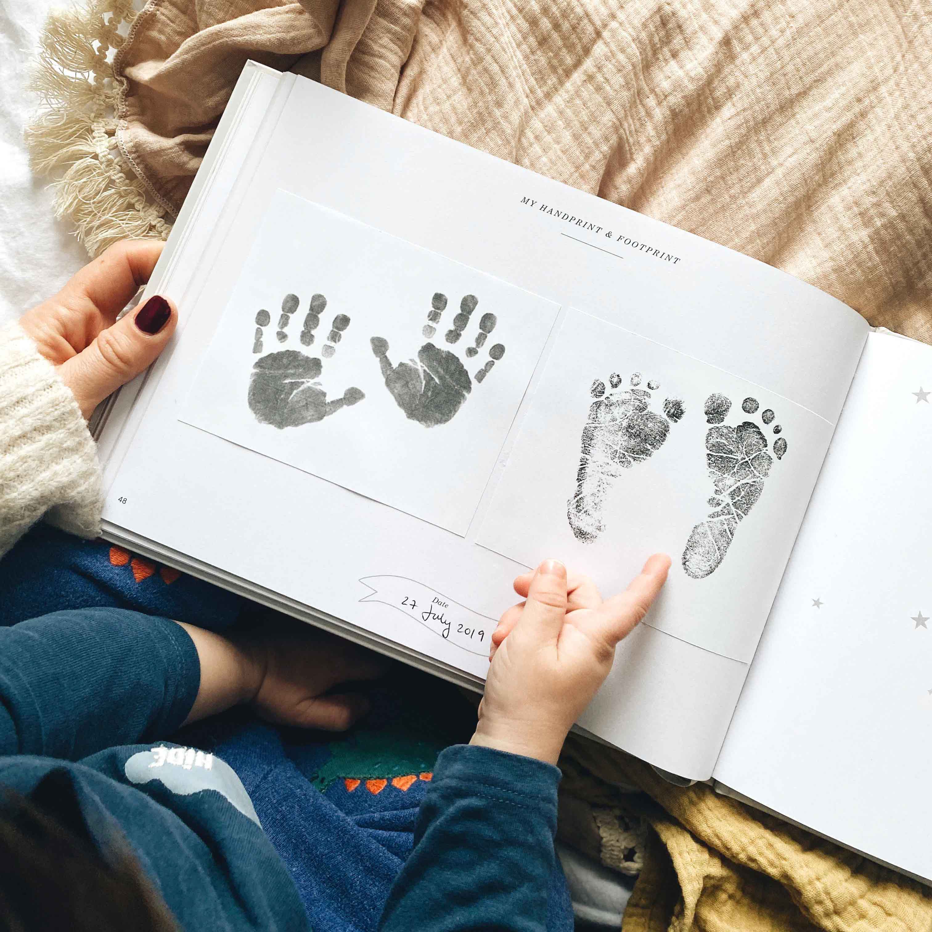 Child's hand holding an open book with hand and footprints on a soft blanket.