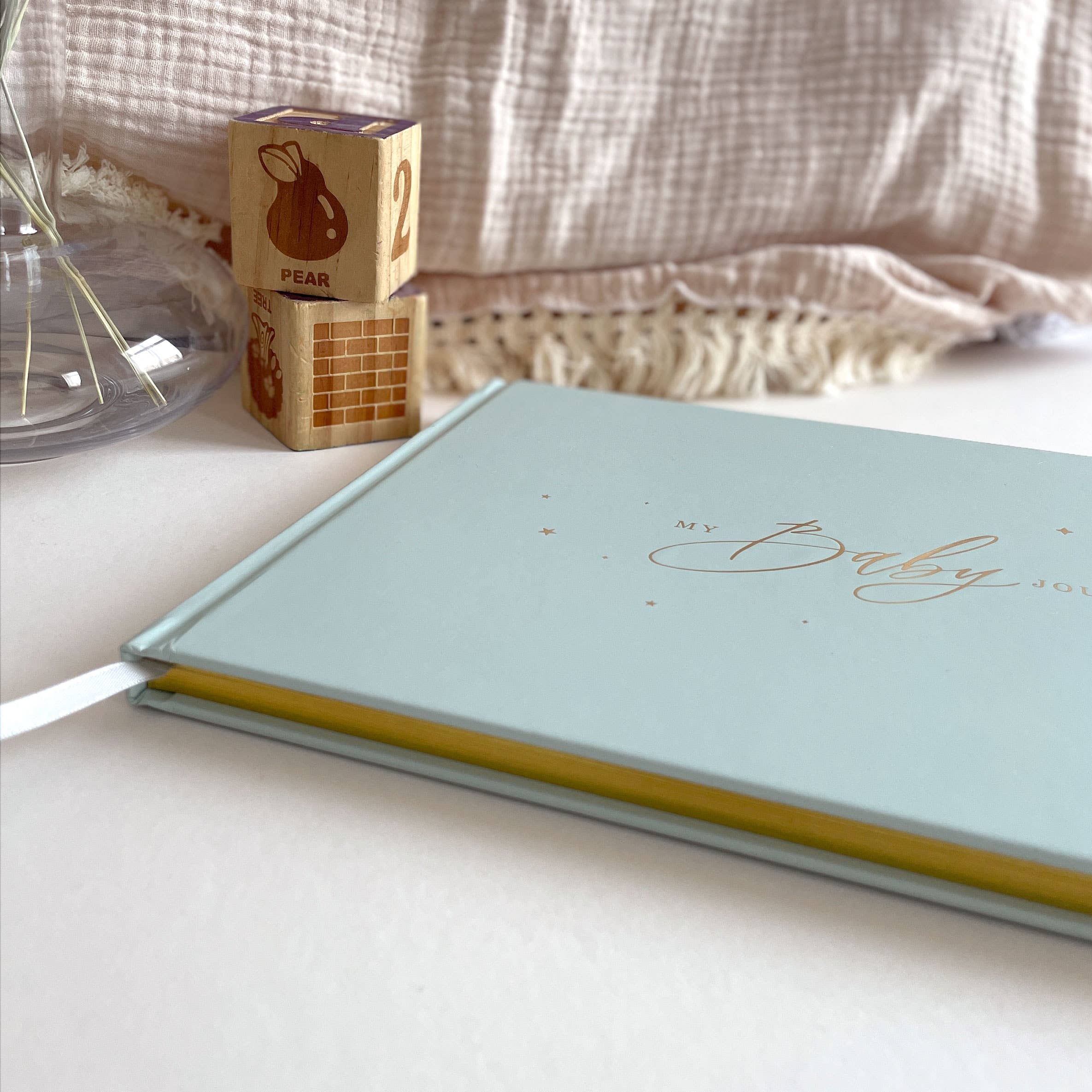 Light blue notebook with 'My Baby' text on a white surface with wooden blocks in the background.