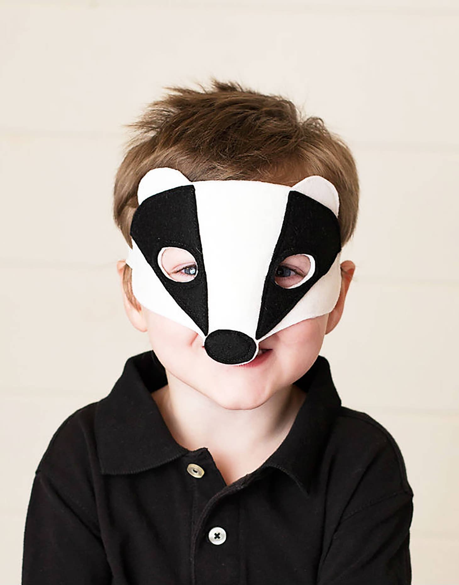 Child wearing a badger mask against a plain background