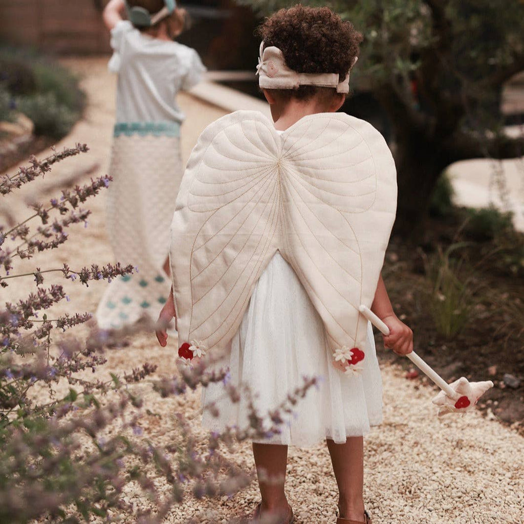 Child wearing fairy set and a white dress standing in a garden with lavender.