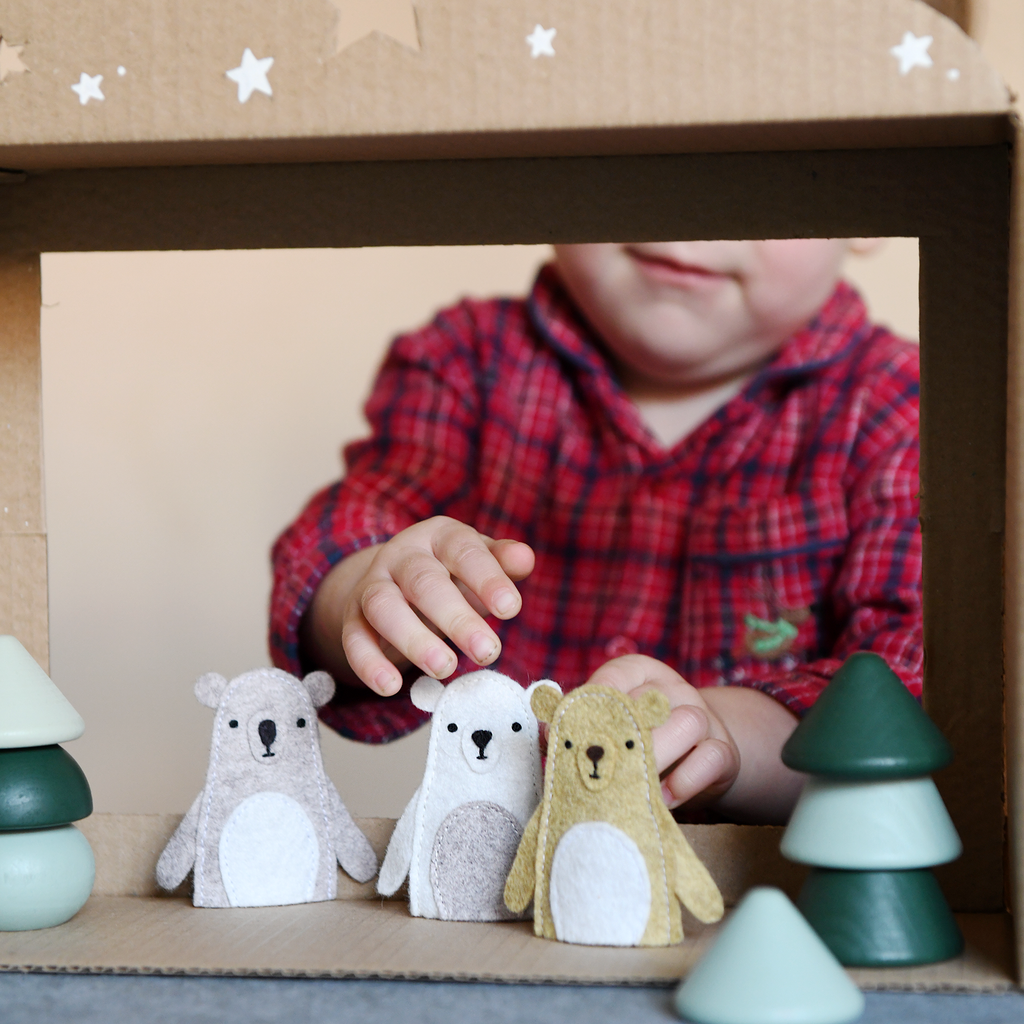 Child playing with toy bears and trees in a cardboard box