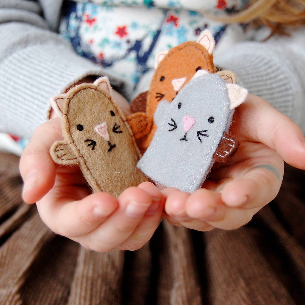 Hands holding three small felt cattoys against a blurred background