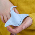 Hand holding a small blue Manta Ray finger puppet against a yellow background