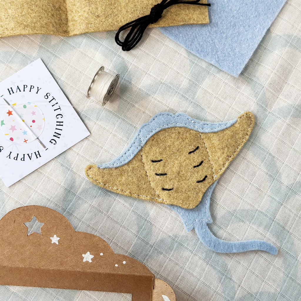 Felt manta ray puppet with a blue tail on a checkered fabric background with sewing supplies.