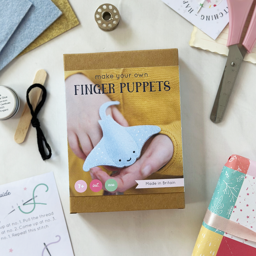 Box for making finger puppets with materials on a white surface