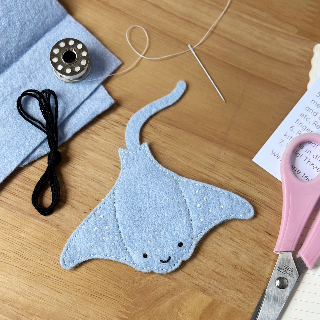 Blue felt mantaray finger puppet with sewing supplies on a wooden surface