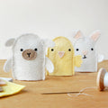 Three felt animal toys on a wooden surface with sewing tools.