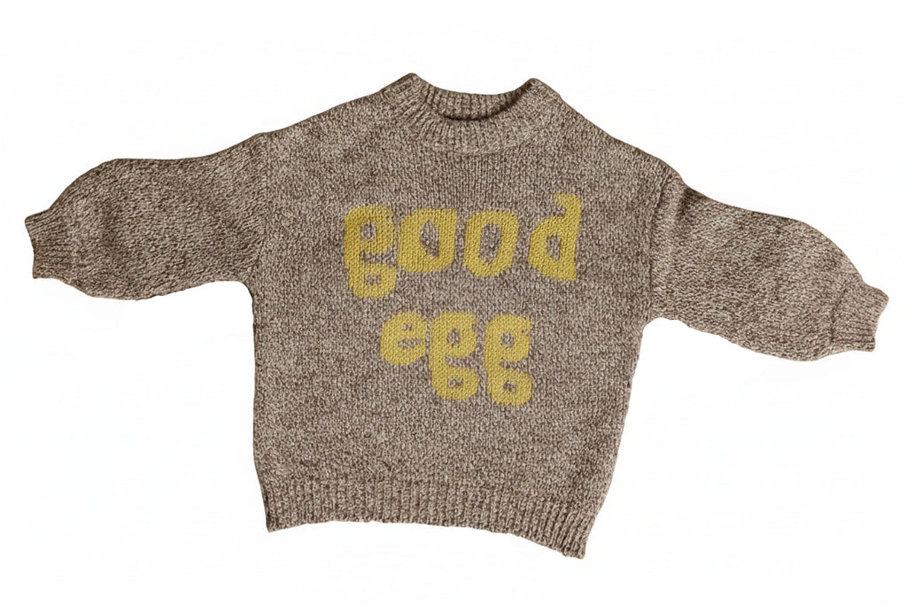 Brown sweater with 'Good Egg' text and egg designs on a beige background