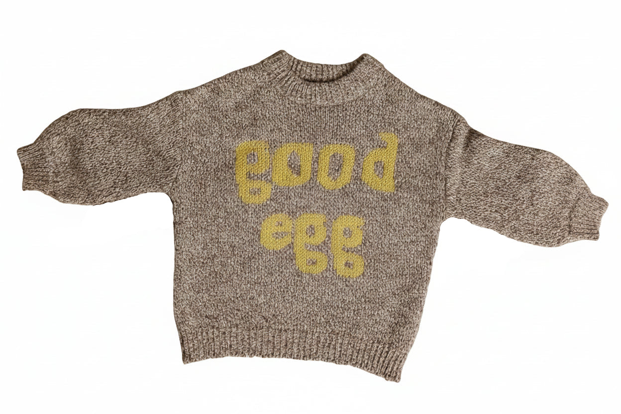 Brown sweater with 'Good Egg' text and egg designs on a beige background