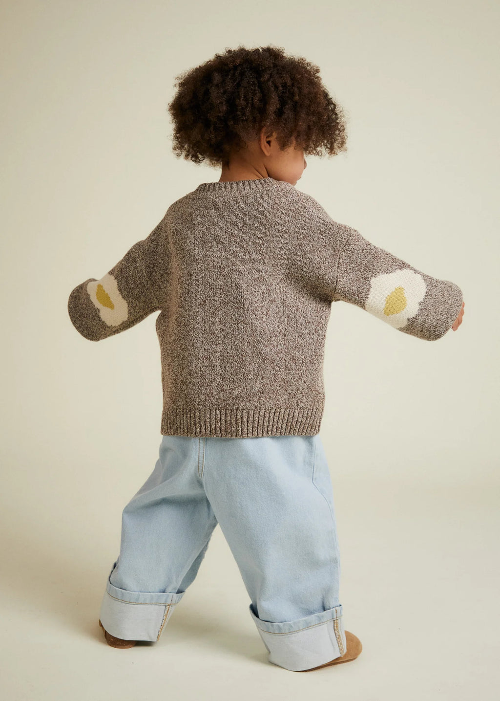 Child wearing a brown knitted sweater with egg patches on a beige background