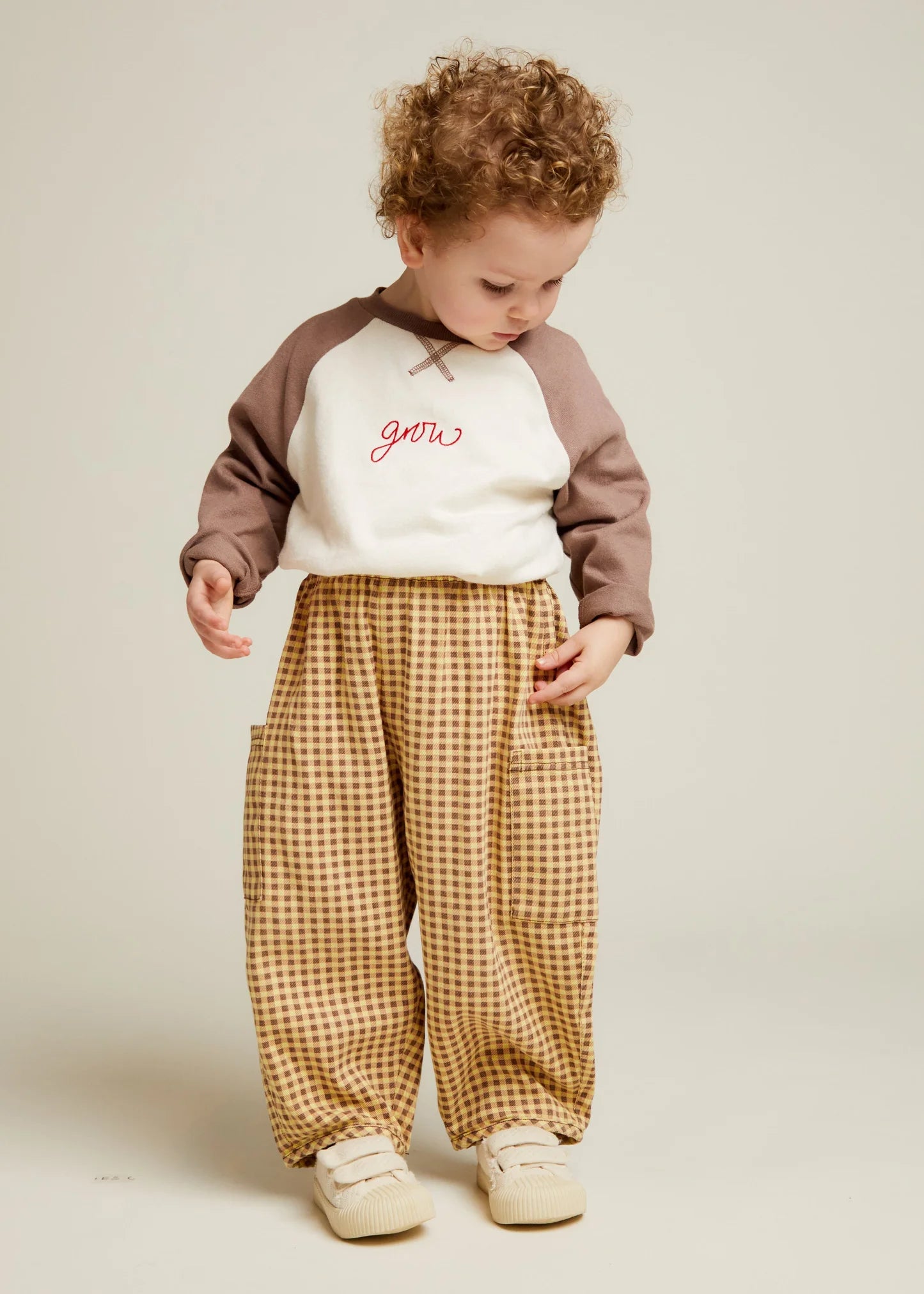 Child wearing a brown and white hoodie with ochre gingham trousers on a beige background