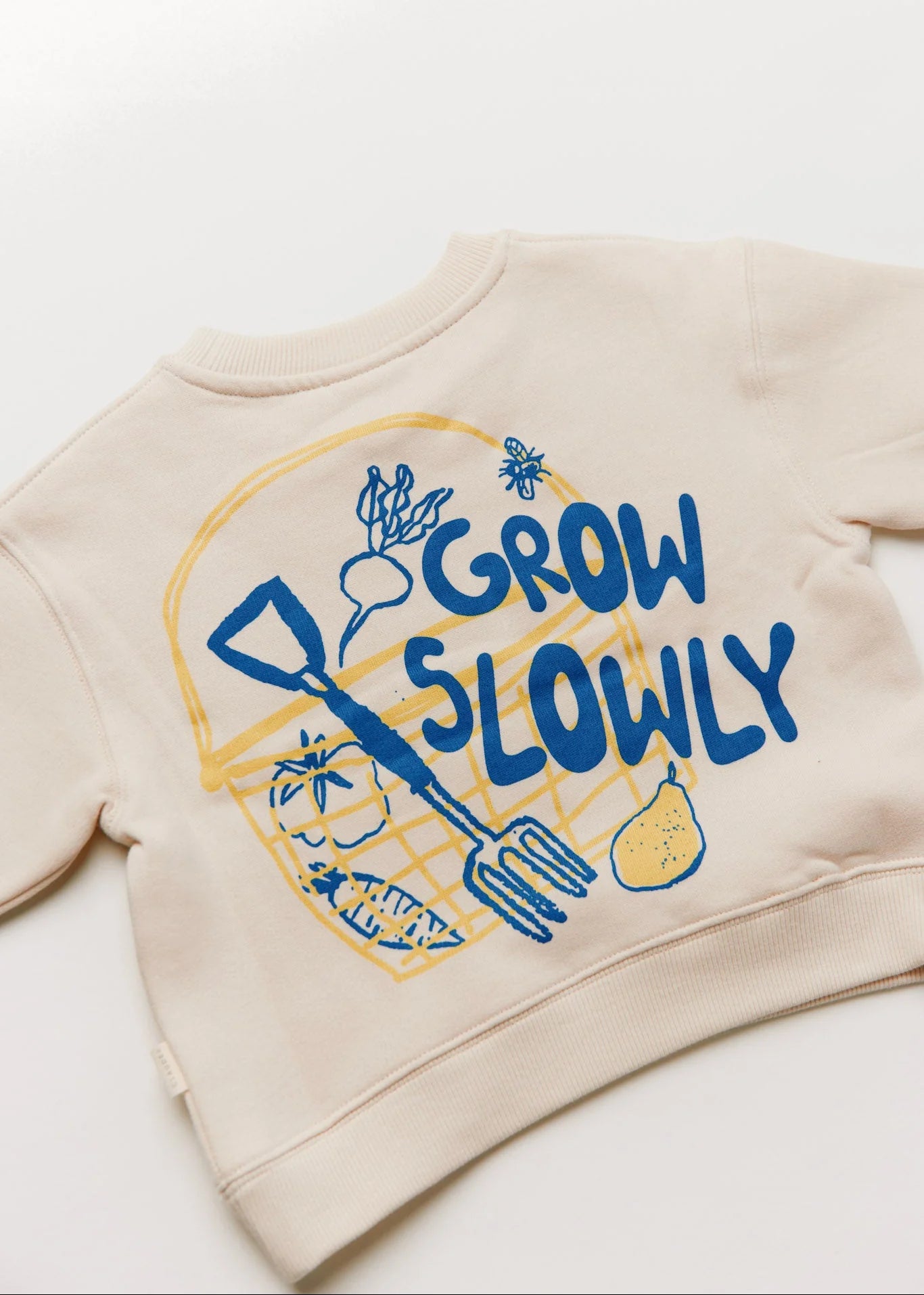 Beige sweatshirt with 'Grow Slowly' text and gardening graphics on a white background