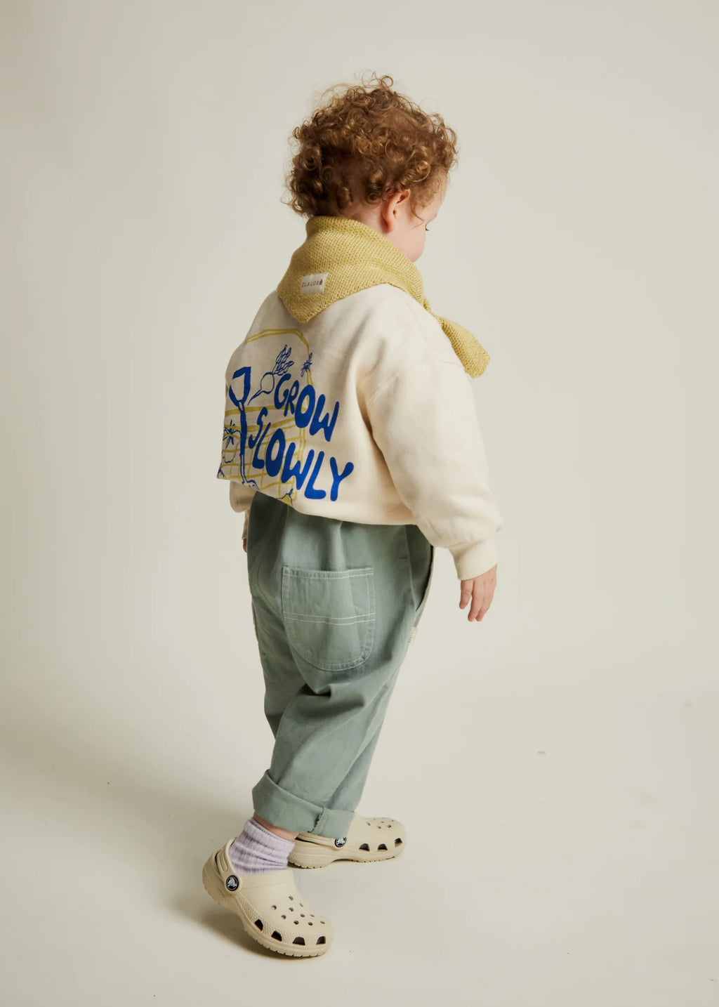 Child wearing a jacket with text, standing on a plain background