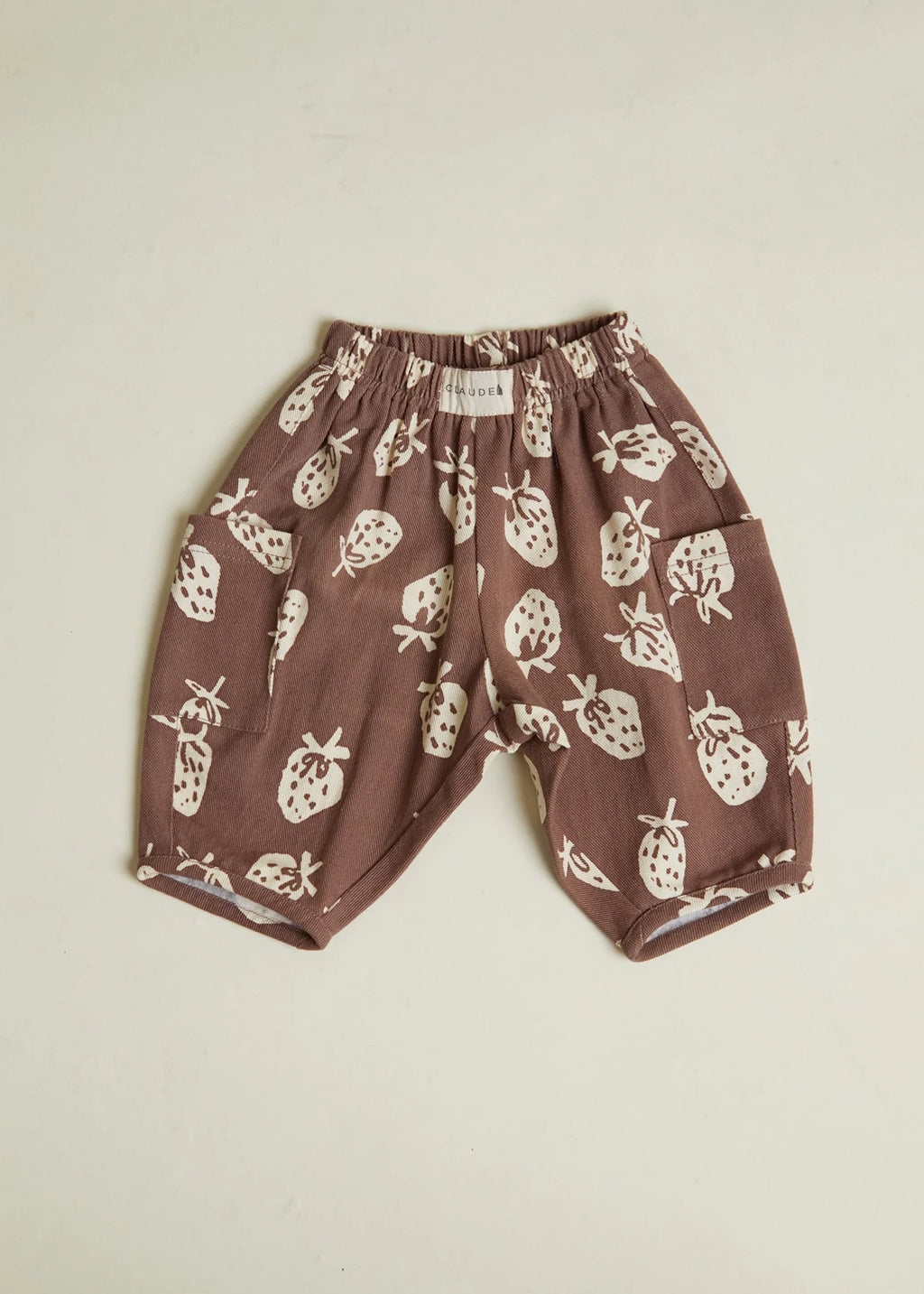 Brown children's pants with white strawberry pattern on a beige background