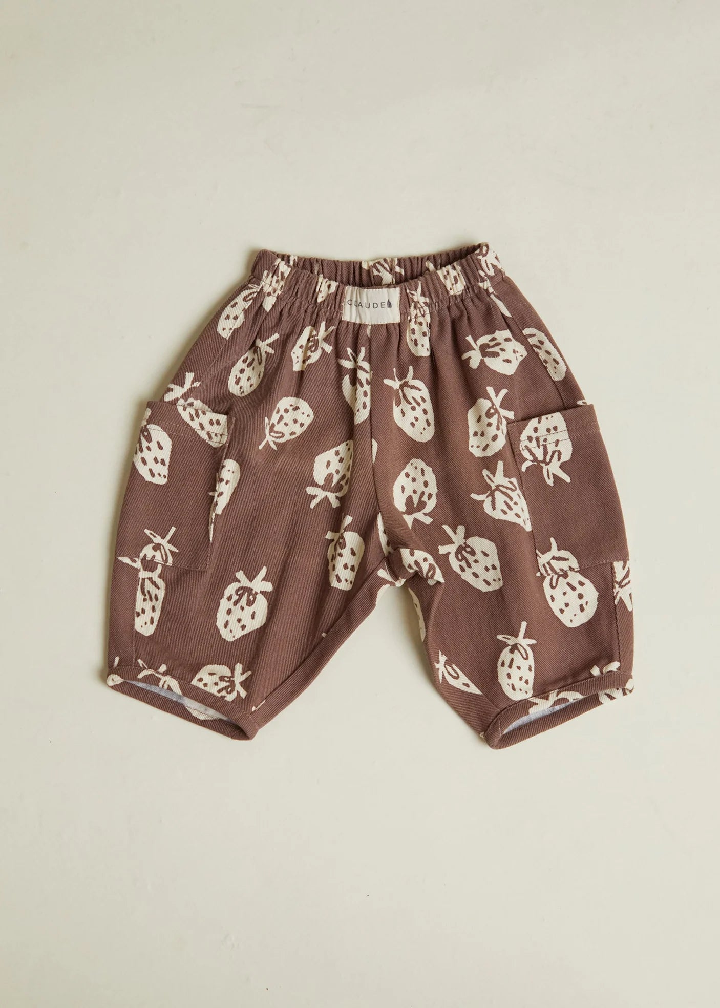 Brown children's pants with white strawberry pattern on a beige background