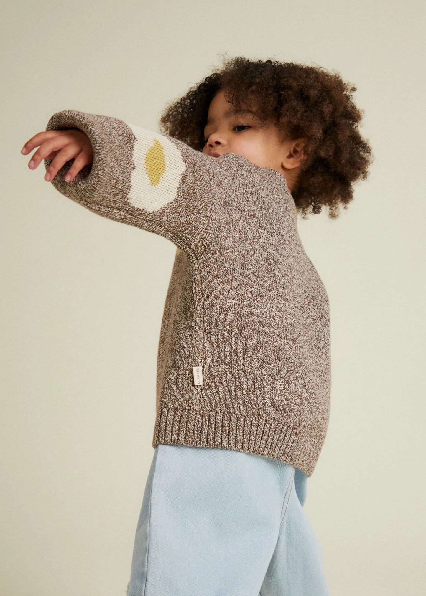 Child wearing a brown knit sweater with a egg design on a plain background