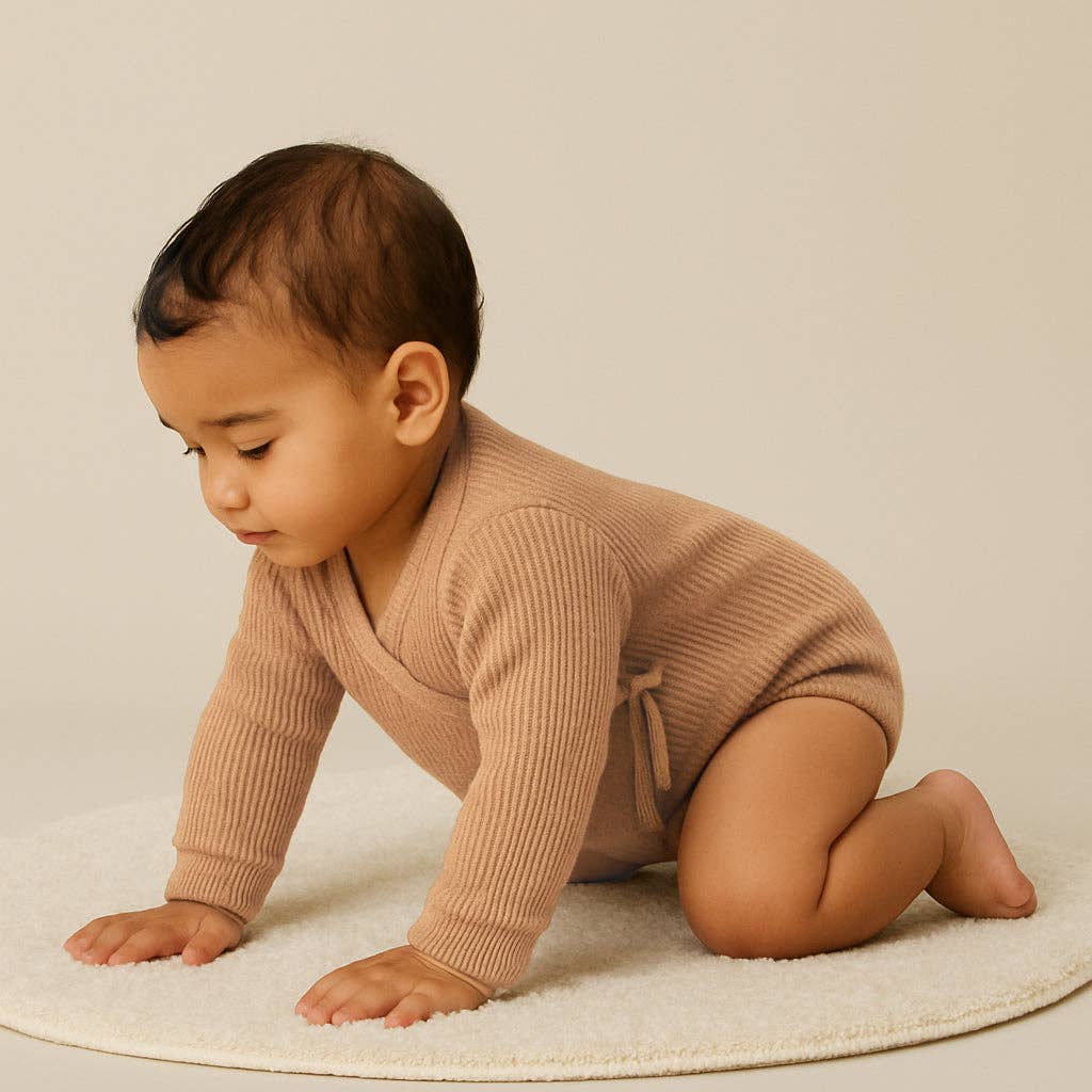 Baby in a beige knitted outfit crawling on a light-colored surface.