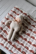 Doll lying on Quilt with scallop pattern in rust and lilac on a white background