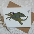 Card with a dragon illustration and a small figure on a textured surface with an envelope.