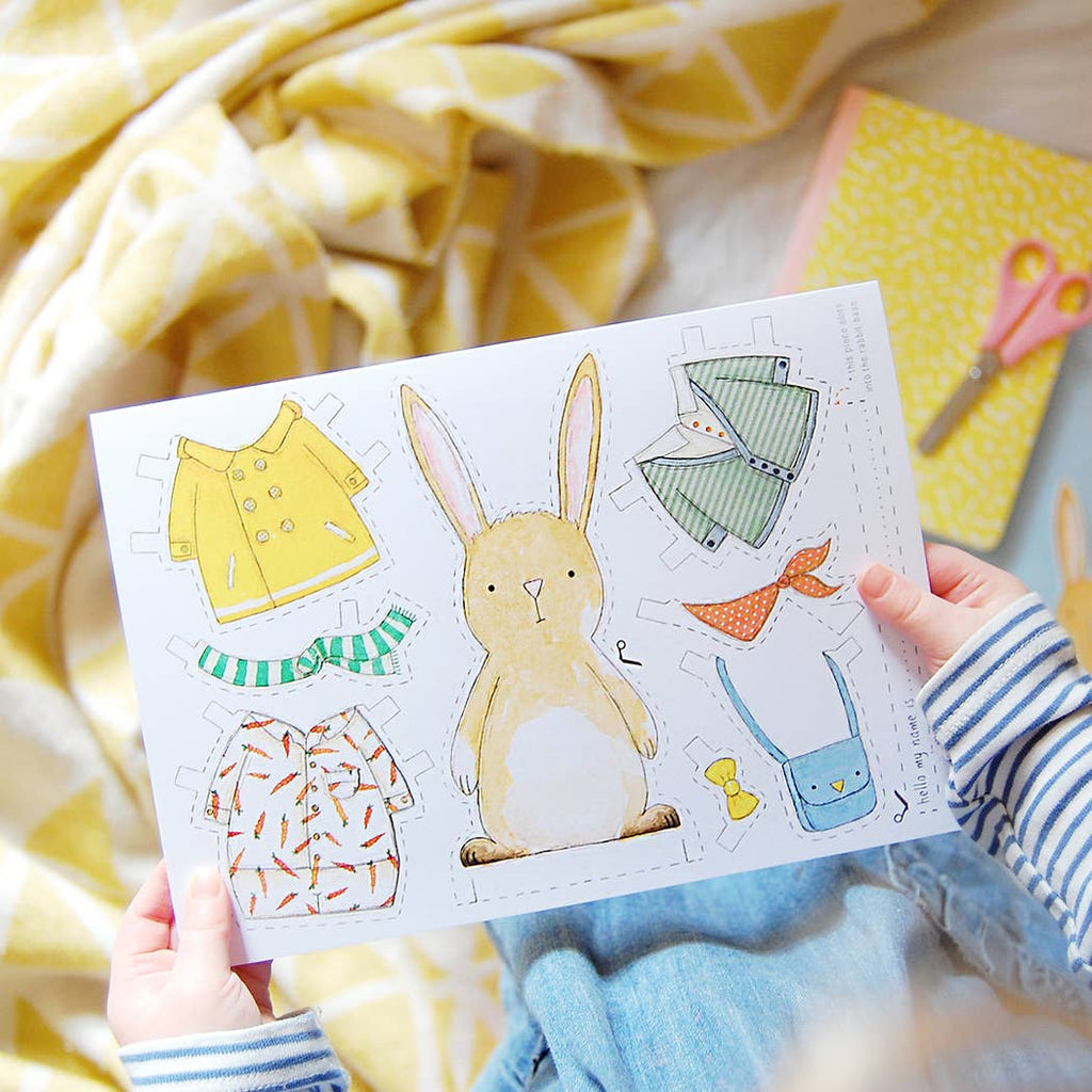Children's paper craft set with a rabbit and clothing items on a yellow blanket.
