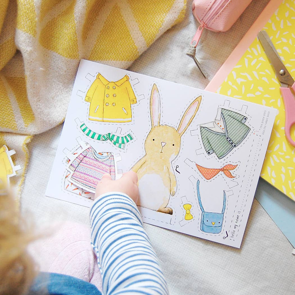 Children's paper craft with a rabbit and clothing items on a blanket