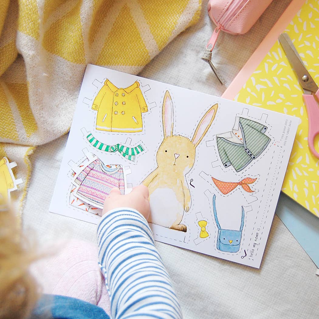 Children's paper craft with a rabbit and clothing items on a blanket