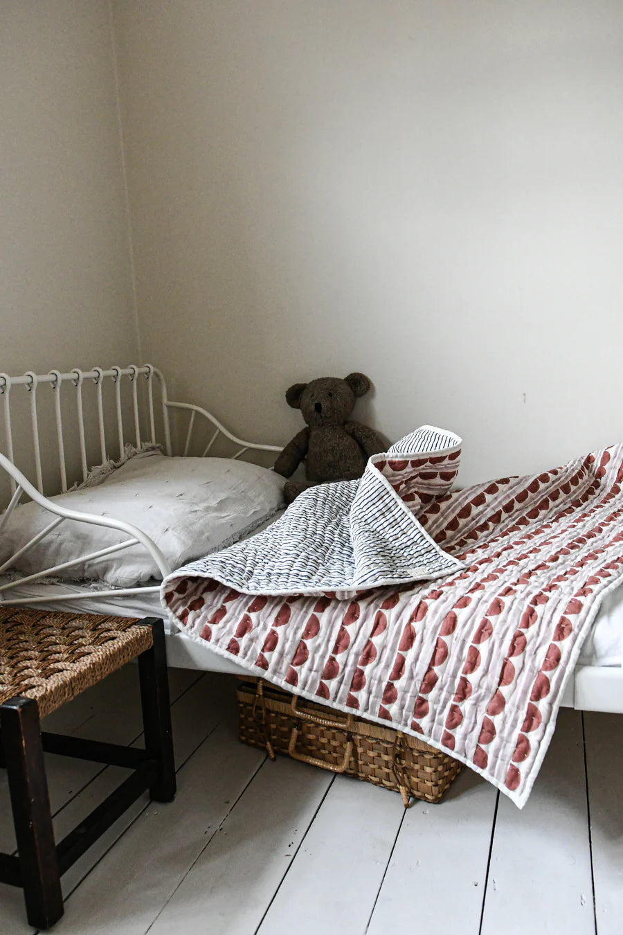 Small bed with a teddy bear and patterned quilt in a cozy room.