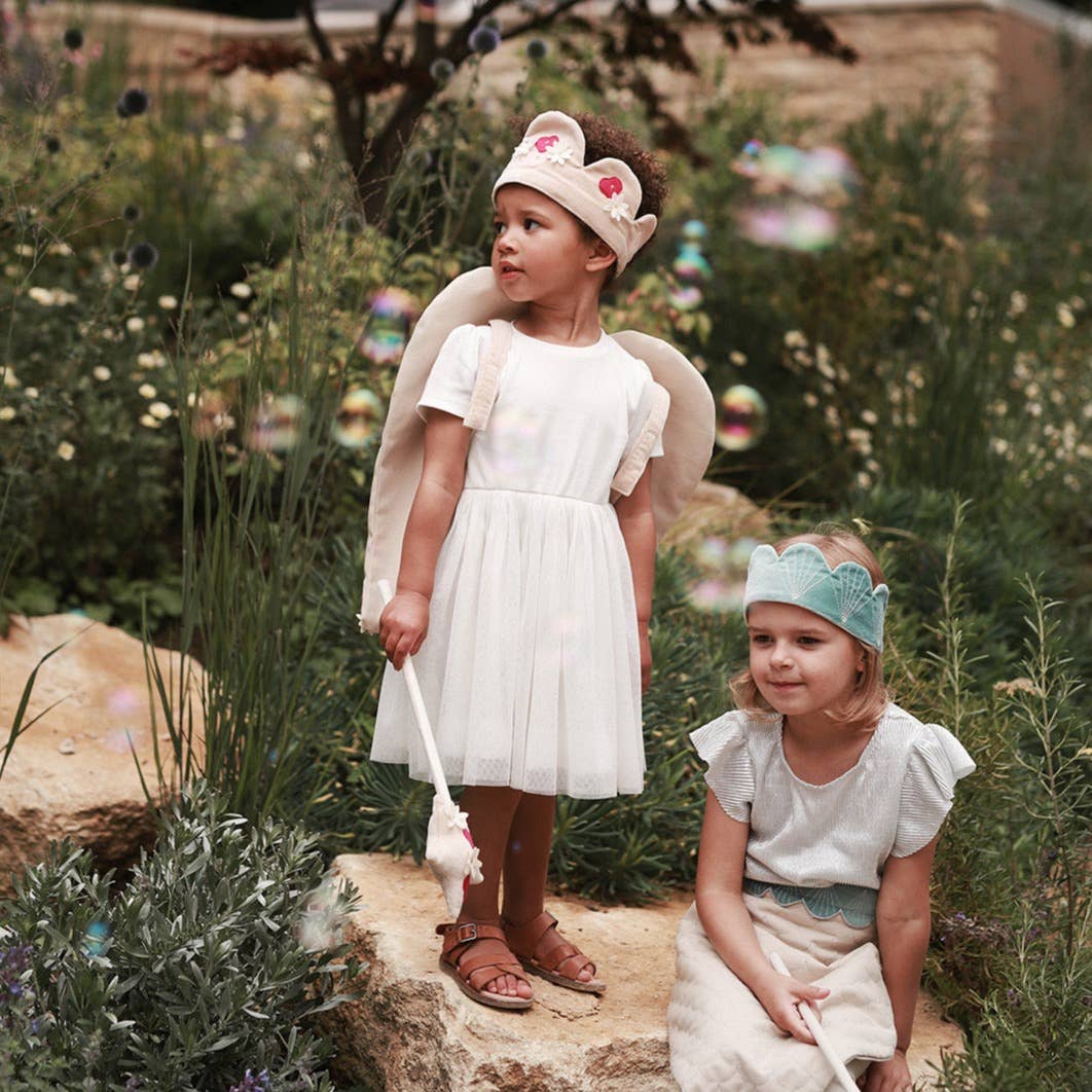 Two young girls in white dresses with floral headbands standing in a garden.