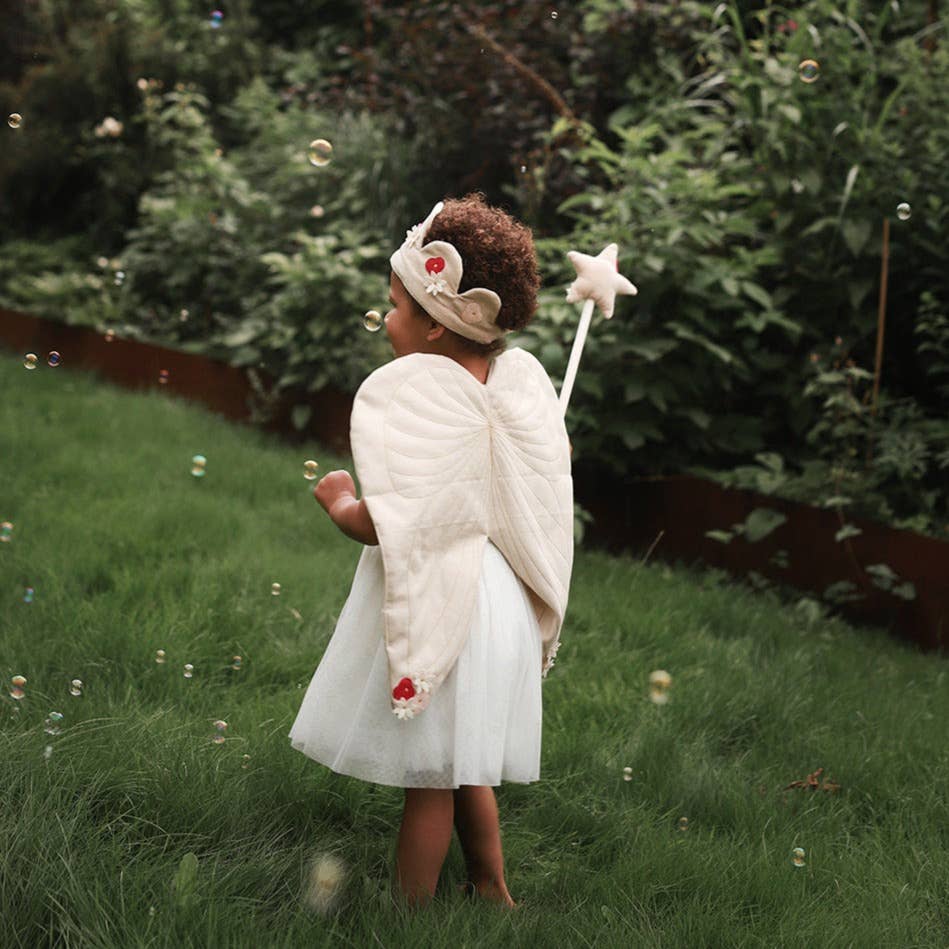 Child in a fairy costume with wings and star wand standing in a grassy area with bubbles.