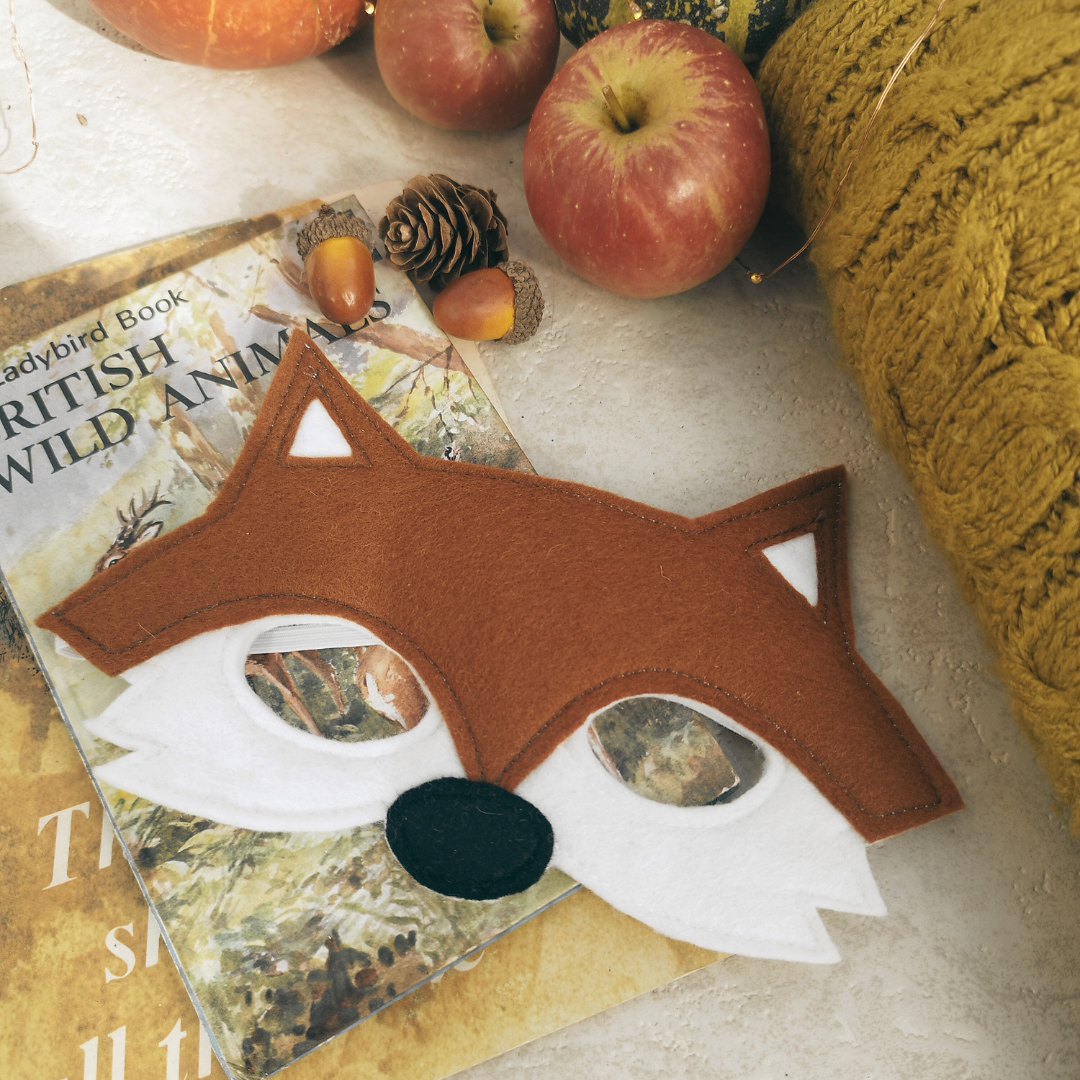 Fox mask on a magazine with apples and pinecones in the background