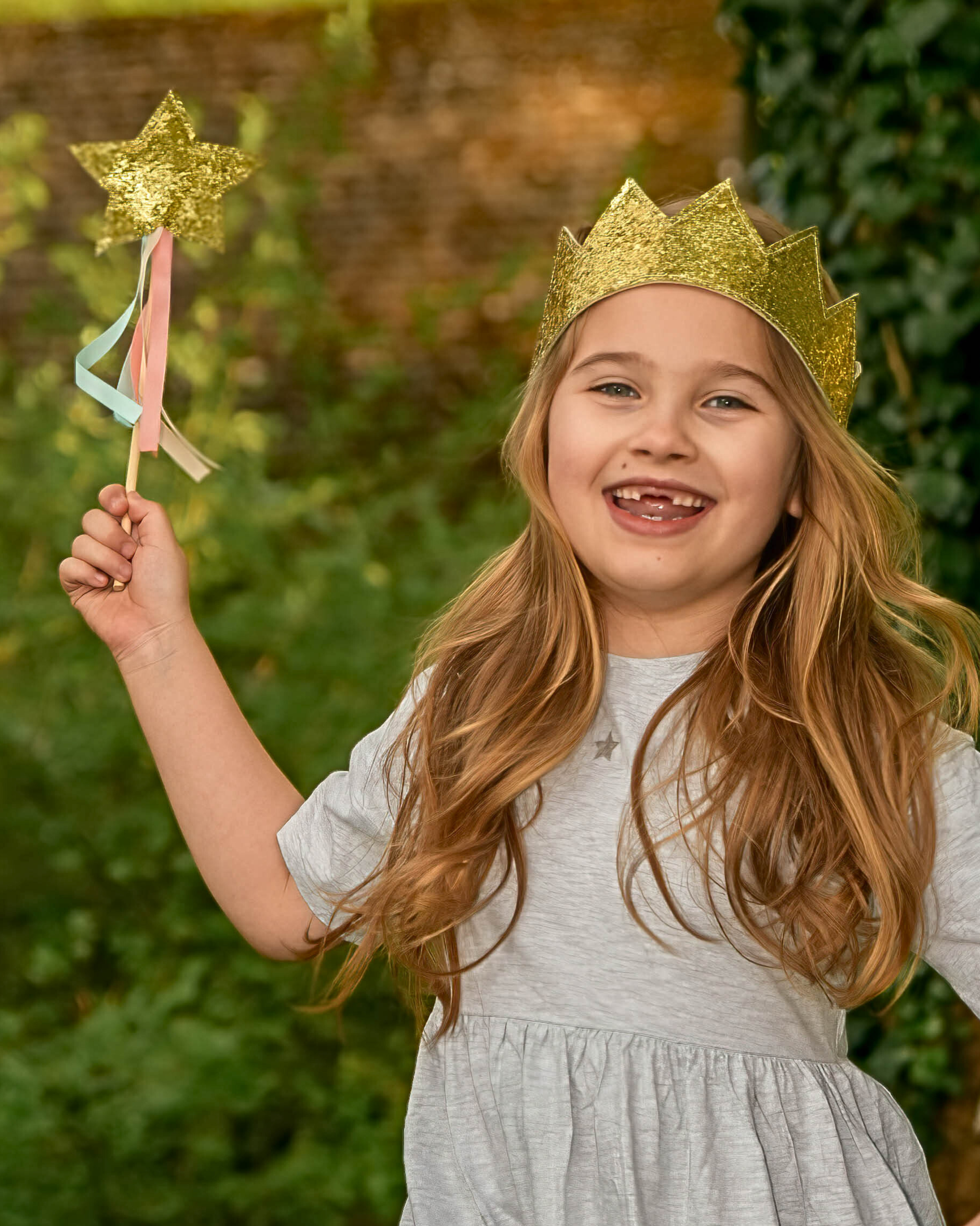 Young girl wearing a gold crown and holding a star wand with a blurred green background