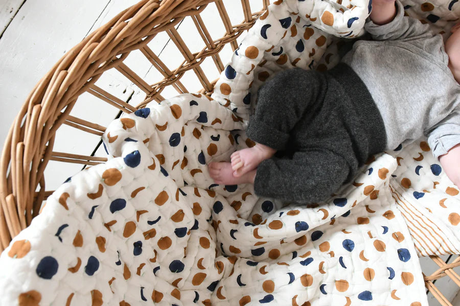 Baby lying on a moon patterned quilt in a wicker crib
