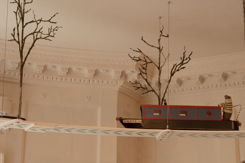 Decorative model of a boat with branches on a shelf against a beige wall.
