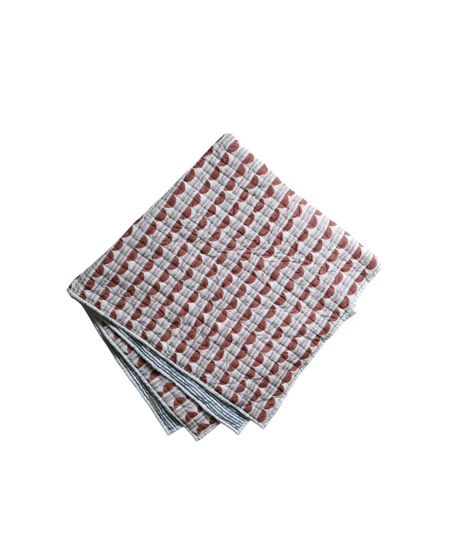 Quilt with scallop pattern in rust and lilac on a white background