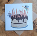 Greeting card with a birthday cake illustration featuring candles and fairies on a wooden surface.