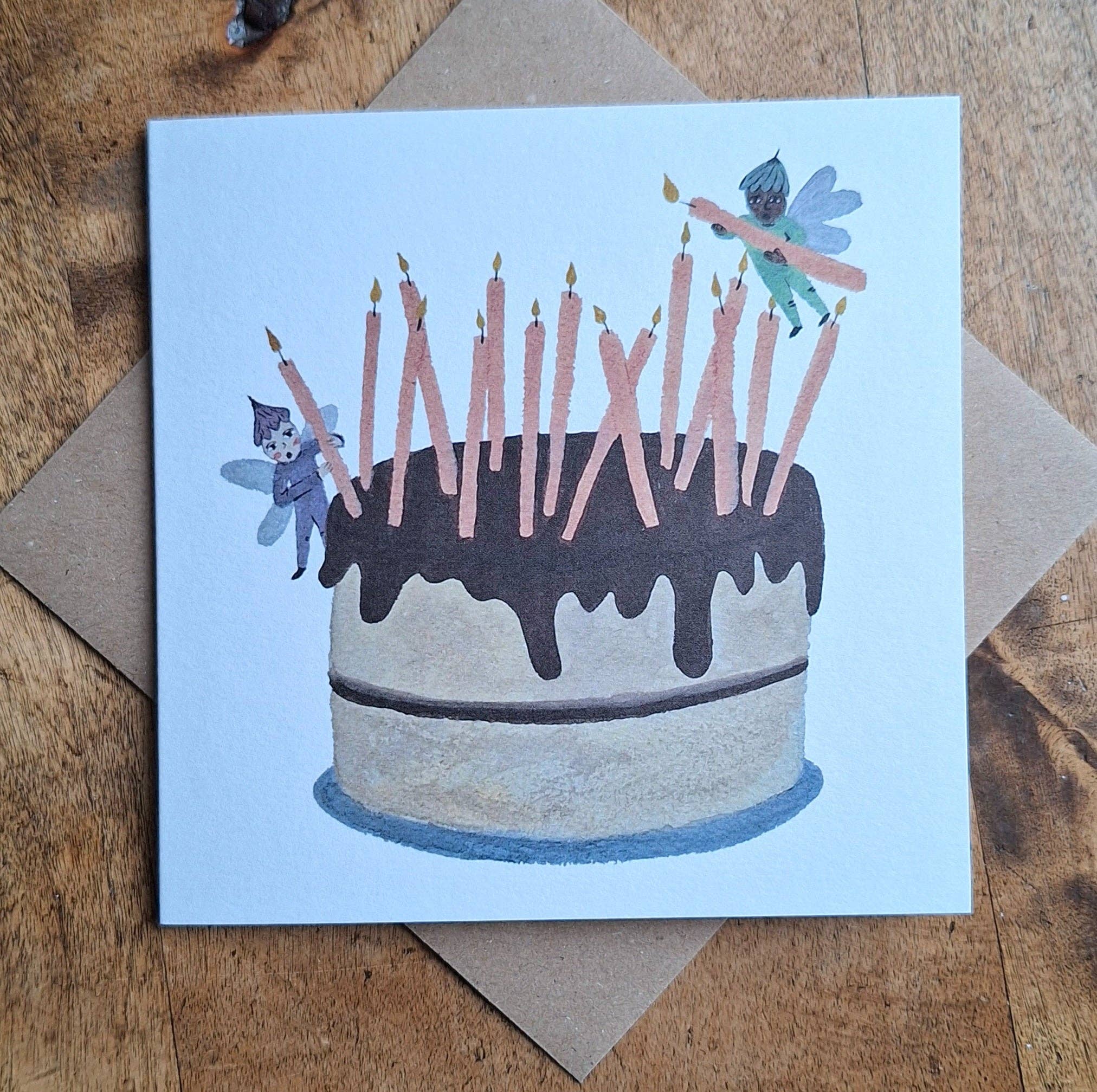Greeting card with a birthday cake illustration featuring candles and fairies on a wooden surface.