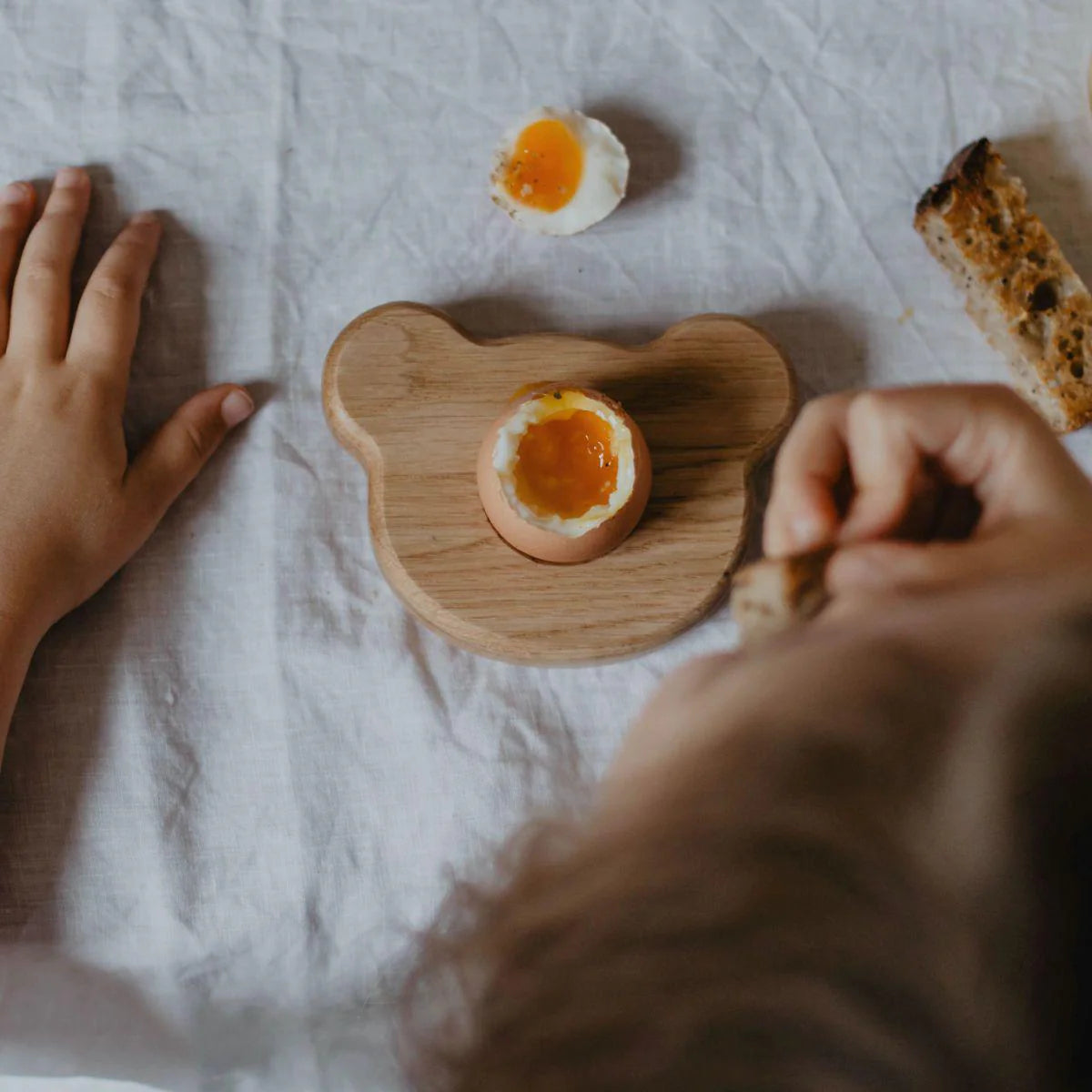 Person holding a soft-boiled egg on a wooden board with a blurred background