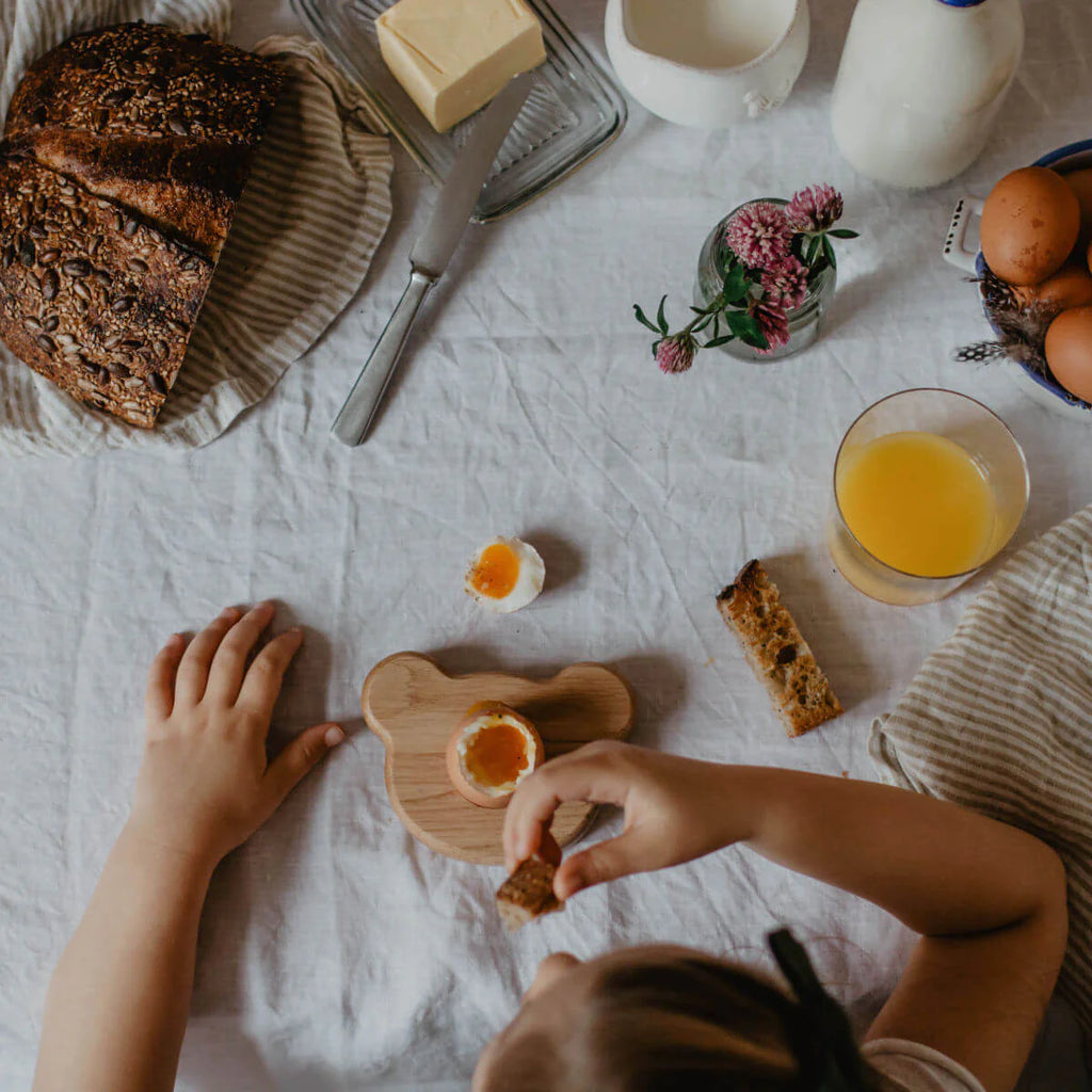 Two people eating breakfast at a table with bread, butter, milk, and juice.